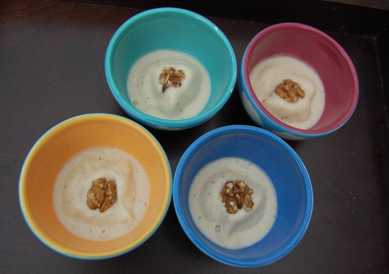 Four colorful bowls of homemade banana ice cream with pecans on top.