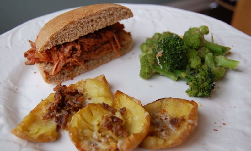 Pulled pork bbq on a whole-wheat bun, broccoli, and potato skins on a plate.