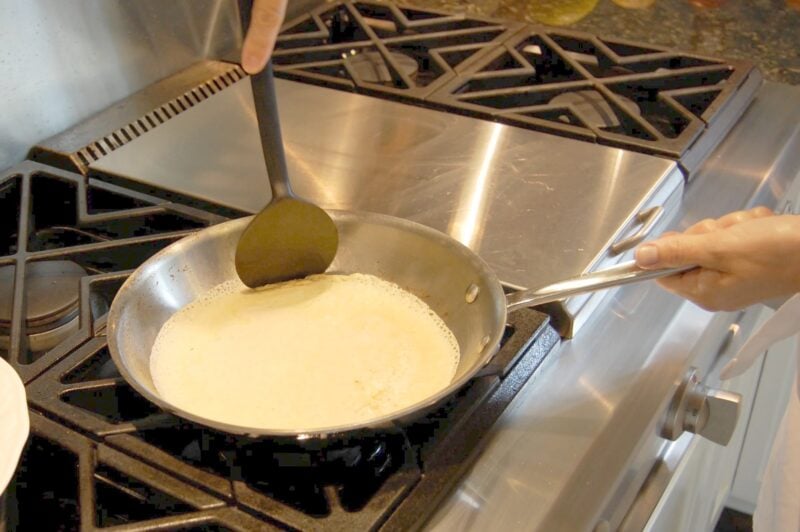 Pushing down the edges of whole wheat crepe batter in a frying pan