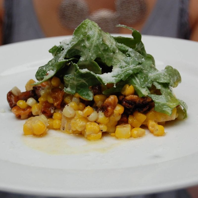 Well plated corn and arugula topped with a sprinkle of cheese.
