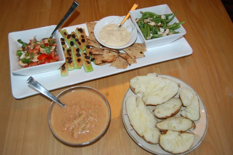 Crackers and hummus, baked potatoes, green beans, and a bowl of gazpacho plated on the dinner table.