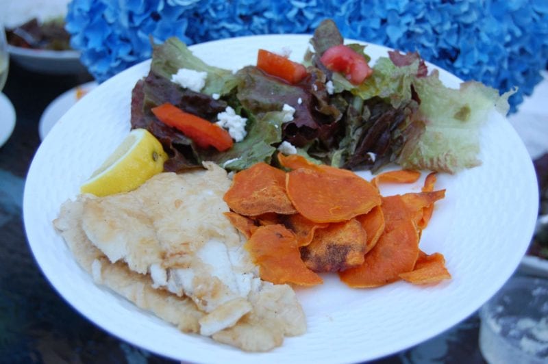 Baked sweet potato chips, sautéed fish, and a salad on a plate.