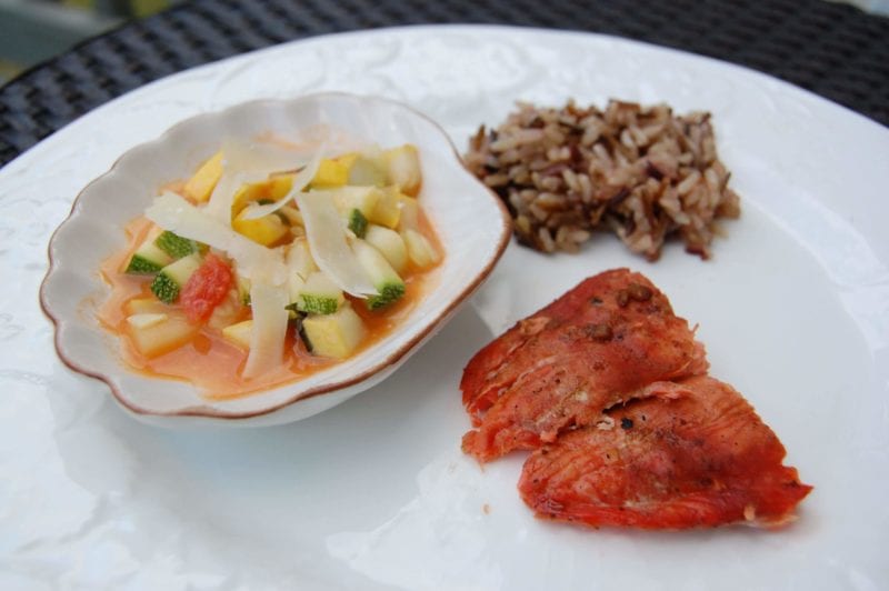 Teriyaki salmon, squash, zucchini, tomatoes topped with Parmesan, and a side of wild rice on a plate.