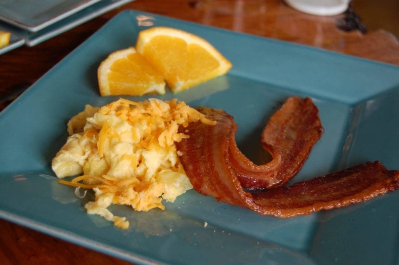 Two pieces of bacon, scrambled eggs with cheese, and a side of orange slices from Halcyon in North Carolina.
