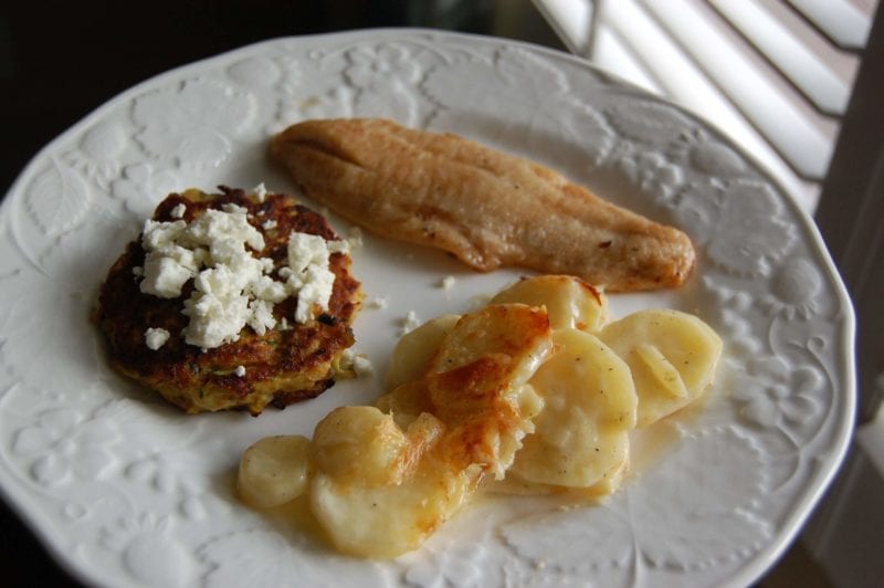 Fish, squash fritters topped with goat cheese, and potato gratin on a plate.