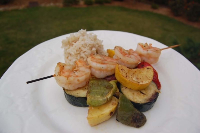 Shrimp & vegetable kabobs over brown rice on a plate.