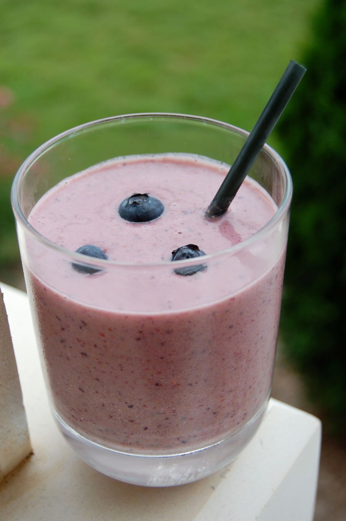 PB & J smoothie in a glass with straw and blueberries