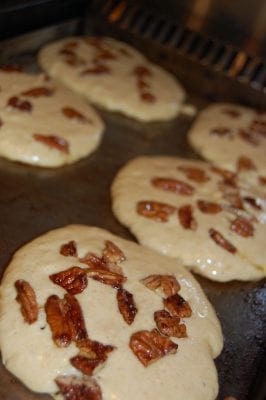 Banana pancakes with pecans in them cooking on the stove.