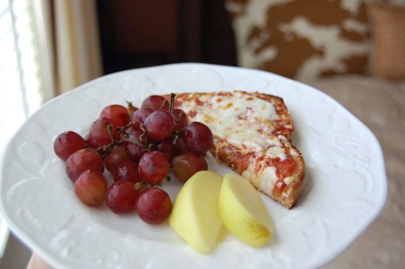 Homemade toast pizza with a side of grapes and apples on a plate.