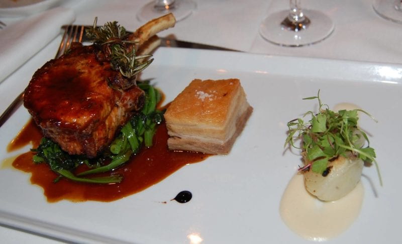 Pork chop on a bed of greens on a plate served at Gotham Bar & Grill in NYC.