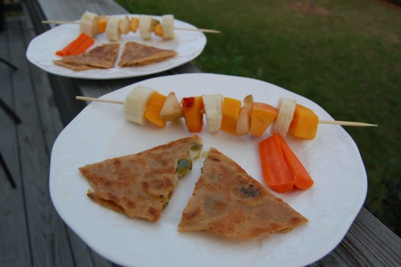 Homemade quesadillas and fruit kabobs on a plate.