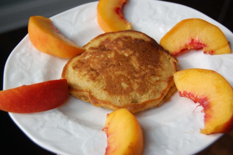 Homemade banana pancakes with sliced peaches around it in the shape of a sunshine.