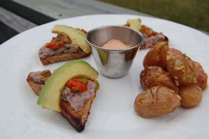 Open-faced sandwich with black bean hummus, bell peppers, and avocado with a side of roasted potatoes and mango.