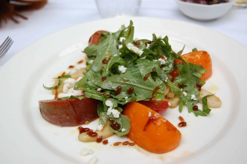A small plate of arugula, sliced fruit pieces, blue cheese crumbles and dressing.